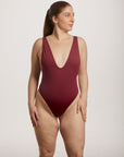 Woman wearing a burgundy swimsuit against a plain background